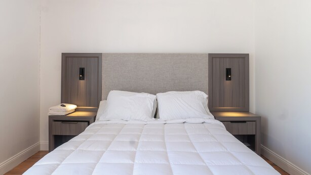 Una cama bien hecha con un edredón blanco acolchado, dos mesitas de noche con lámparas y un cabecero con iluminación.