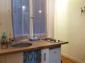 A small kitchen with a sink, a window with curtains, a bottle of hand soap, and a tissue box. - Cozy mini-studio for 2 near the Louvre, metro, and elevator (Paris)