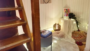 A room with a wooden staircase, a white wall with a line drawing, a small table with a vase, a colorful rug, and a white blanket on the floor. - Cozy Mini-Studio for 2 Near Louvre/ Metro/Elevator (Paris)