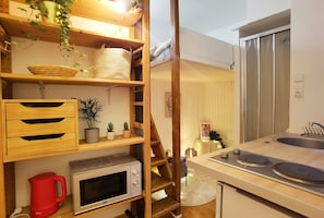 A compact kitchen with wooden shelves, a microwave, a red kettle, and a stainless steel refrigerator. - Cozy mini-studio for 2 near the Louvre, metro, and elevator (Paris)