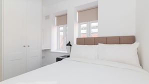 A bedroom with a bed, white wardrobe, and a window with blinds. - Dean Swift Square (Dublin)