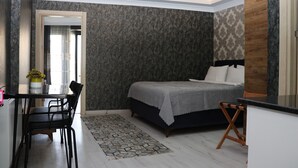 A bedroom with a bed, a desk, and a chair. There is a window with curtains, a radiator, and a small table with a plant. - DT SUITES  (İstanbul)