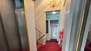 A hotel corridor with a red carpet, a chandelier, and a fire extinguisher. - DT SUITES  (İstanbul)
