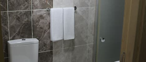 Een badkamer met toilet, prullenbak, douchecabine van glas en een wastafel.