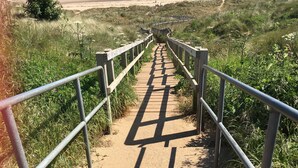 Une promenade en bois, bordée de rampes métalliques, qui mène à une plage.