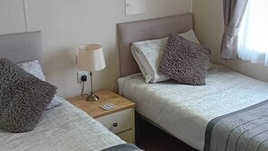 Une chambre d’hôtel avec deux lits, une table de chevet avec une lampe, un tableau au mur et une fen être avec des rideaux.