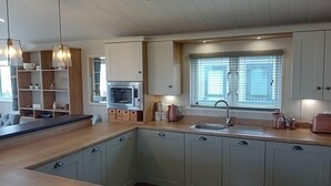 Une cuisine moderne avec des meubles de couleur vert clair, un four encastré, un évier et une fenêtre équipée de stores.
