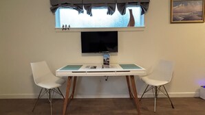 Ein Zimmer mit Esstisch, zwei Stühlen, einem flachbildfernseher über dem Tisch, einem Fenster mit Aussicht und einem Gemälde an der Wand.