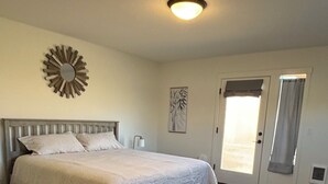 Ein Schlafzimmer mit einem Bett, Holzboden, einer Deckenleuchte, einer Tür und einem an der Wand befestigten Spiegel.