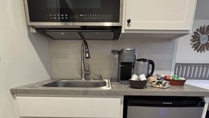 Eine kompakte Küche mit Mikrowelle aus Edelstahl, integriertem Geschirrspüler, Spüle und Kaffeemaschine.