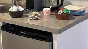 Eine Küchenarbeitsplatte mit Kaffeemaschine, Wasserkocher, einer Schüssel mit Snacks, einem Korb mit grünen Lebensmitteln und einem Geschirrgestell.