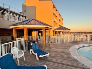 A deck with lounge chairs and a pool, surrounded by a building with balconies. - Sugar Beach 2 Bedroom, 2 Bathroom Condo. Heated Pool. Free Daily Activities! (Orange Beach)