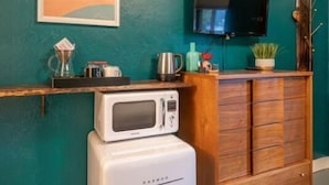 Uma cozinha compacta com micro-ondas, cafeteira e uma prateleira com diversos objetos.