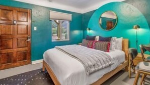 Quarto com uma cama, porta de madeira, janela e espelho redondo na parede.