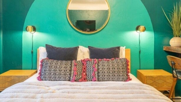 Cama com almofadas estampadas, espelho redondo acima e duas luminárias laterais.