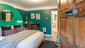 Quarto de hotel com uma cama, uma mesa, um espelho e uma porta com o aviso 'Não Fumar'.