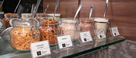 Ein Selbstbedienungs-Frühstücksbereich mit verschiedenen Granola- und Cereal-Optionen, die jeweils mit dem Markennamen gekennzeichnet sind.