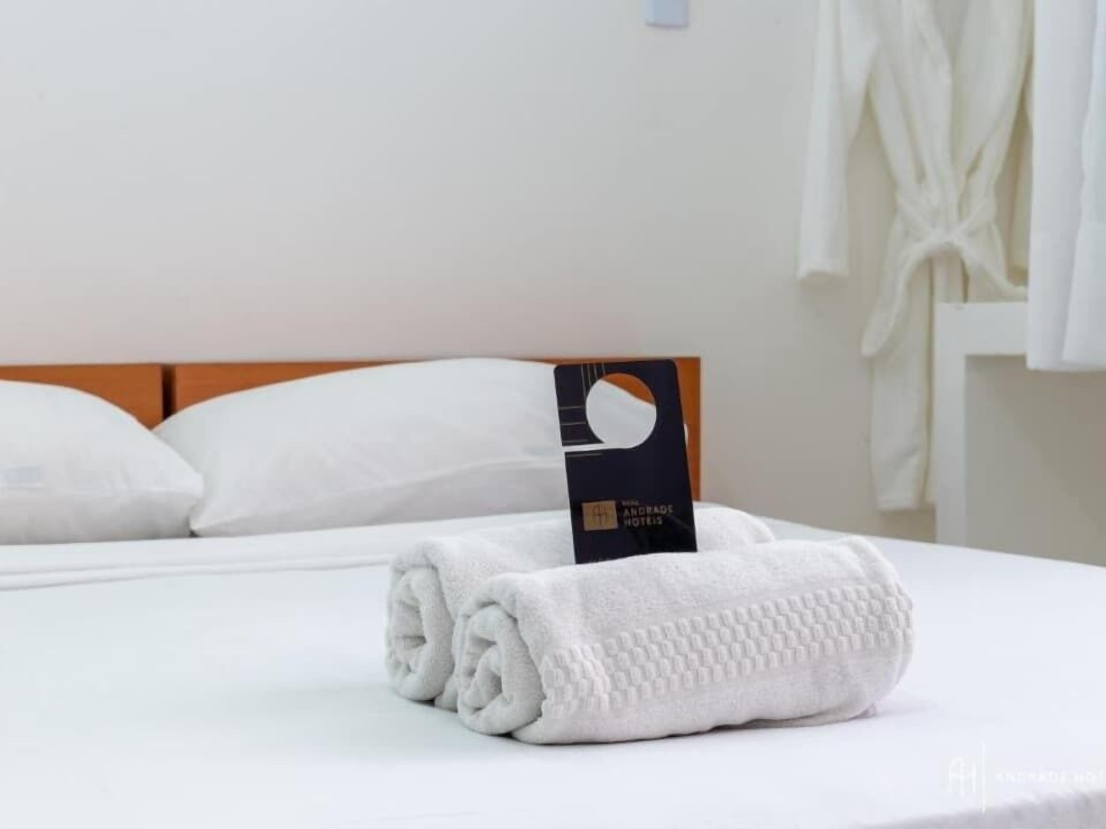 A neatly made bed with a folded white towel and a hotel card on the headboard.