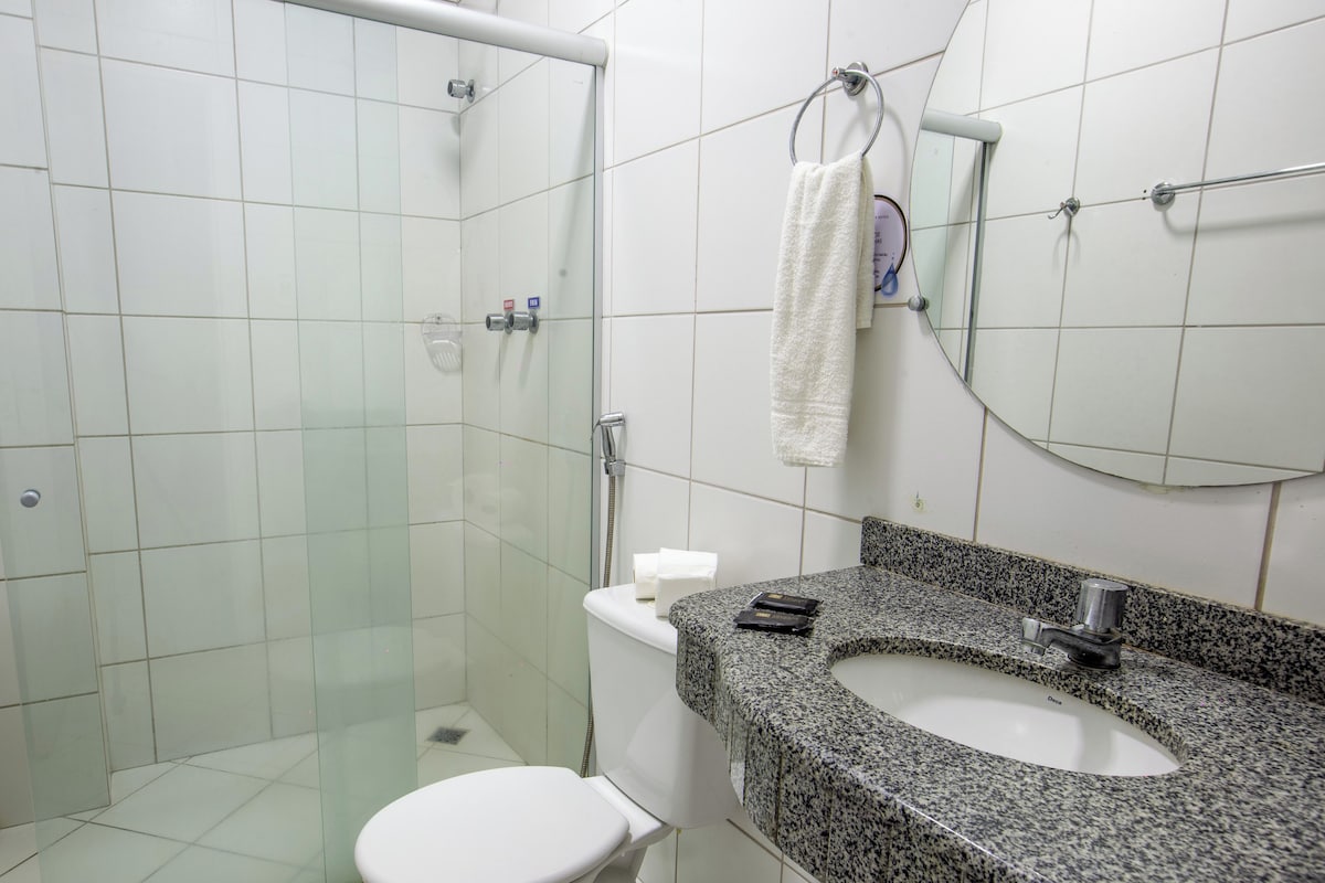 A bathroom with a glass-enclosed shower, a white toilet, and a granite countertop sink.