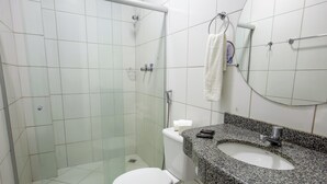 Een badkamer met een glazen douchecabine, een wit toilet, een granieten wastafel en een handdoek aan een metalen handdoekhouder.