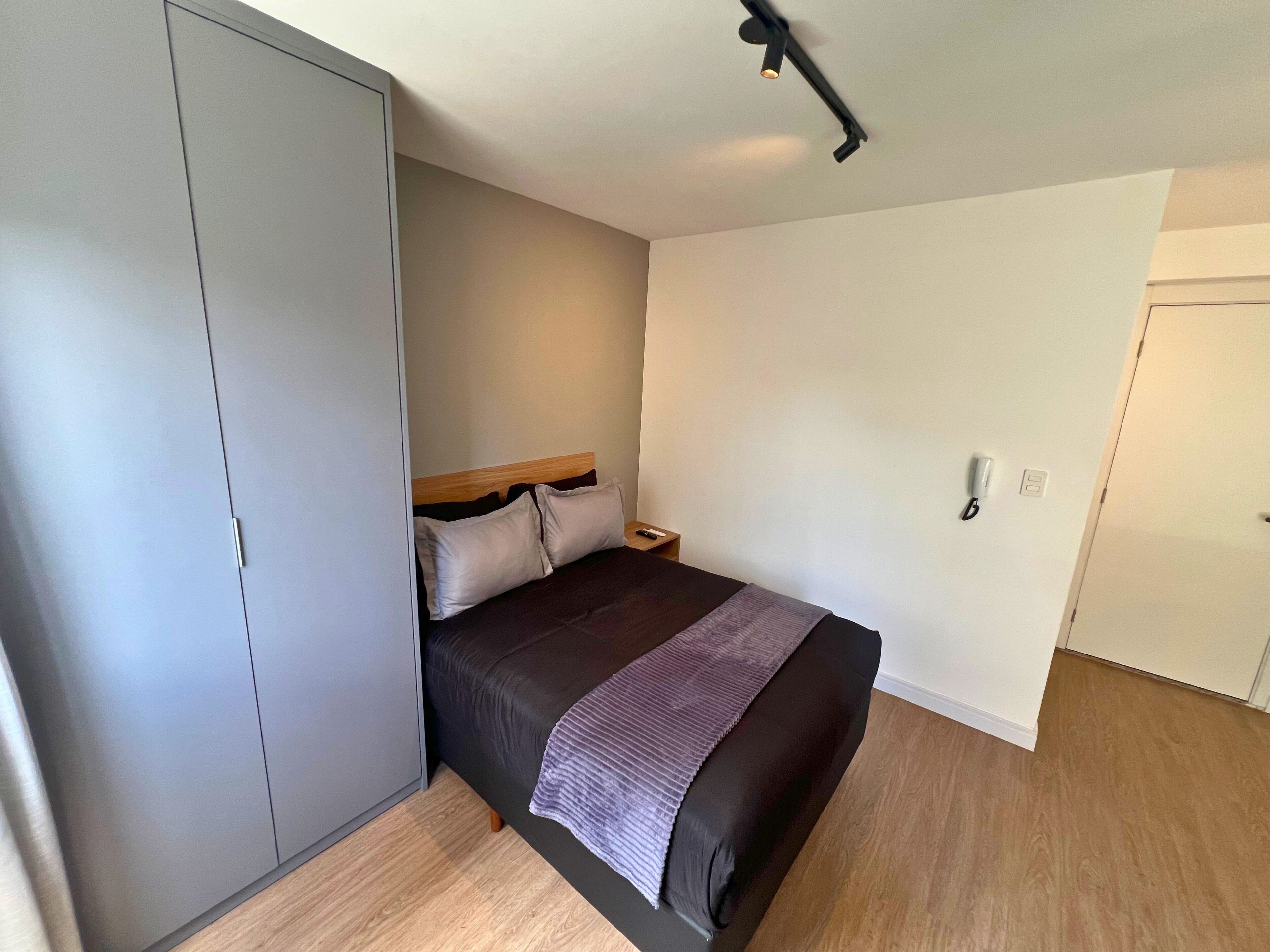 A bedroom with a bed, a wardrobe, a bedside table, and a ceiling light.
