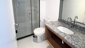 A modern bathroom with a glass shower enclosure, a white toilet, and a granite countertop sink with a mirror. - Hype Vila Mariana (São Paulo)