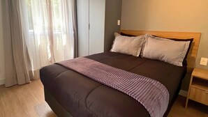 A modern bedroom with a large bed, grey wardrobe, and a wooden nightstand. - Hype Vila Mariana (São Paulo)