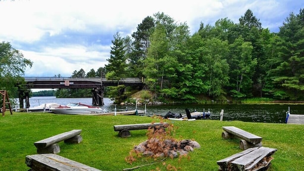 A lakeside park with picnic tables, a small bridge, and boats docked near the water. - Nitschke's Resort Cabin #15 (Minocqua)