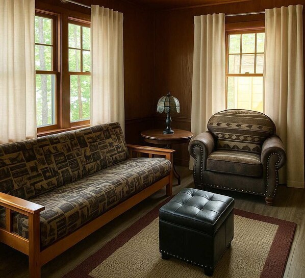 A cozy living room with a patterned sofa, a leather armchair, and a small ottoman. There is a lamp on a side table and a window with curtains. - Gresham Shores - Big Dipper - PET Friendly (Woodruff)