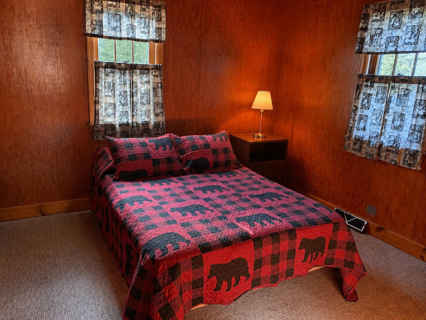 Un dormitorio con cama, mesita de noche, lámpara y cortinas estampadas.