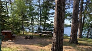 Un terrain de camping équipé de tables de pique-nique, d’un foyer et d’un petit chalet situé au bord d’un lac.