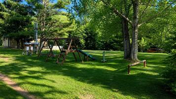 A playground with swings and a slide, surrounded by trees and grass.