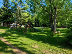 A playground with swings and a slide, surrounded by trees and grass. - Gresham Shores - Big Dipper - PET Friendly (Woodruff)