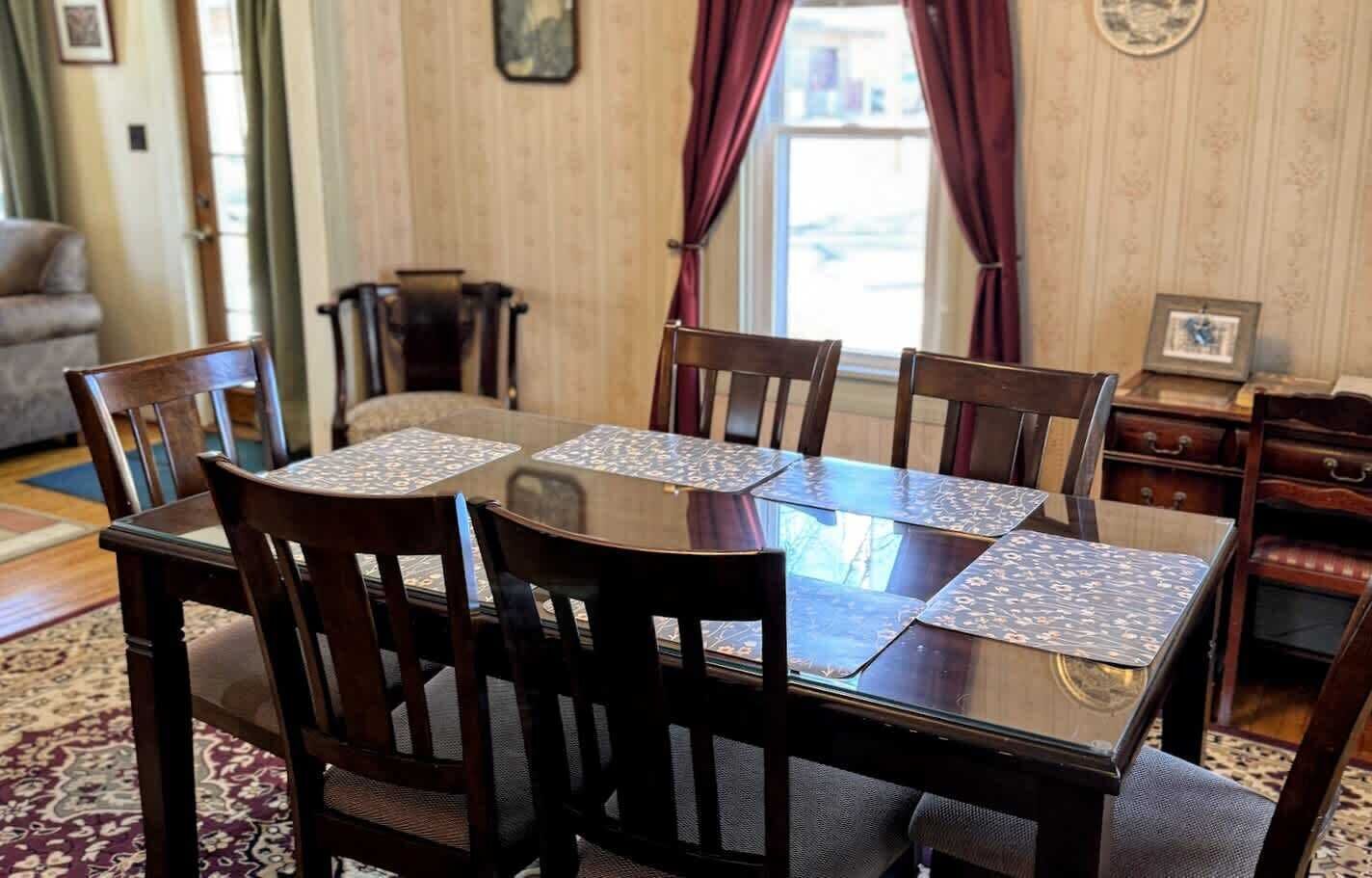 A dining area with a round table and six chairs, a patterned rug, and a wooden cabinet with drawers.