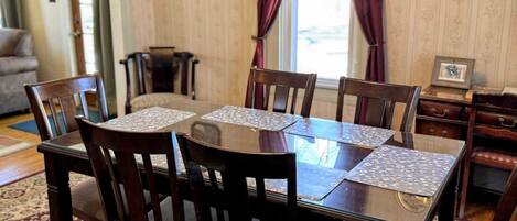 A dining area with a round table and six chairs, a patterned rug, and a wooden cabinet with drawers.