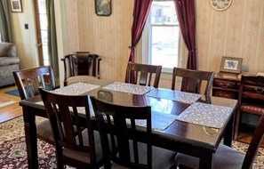 A dining area with a round table and six chairs, a patterned rug, and a wooden cabinet with drawers. - Margeson House -pet Friendly Home (Minocqua)