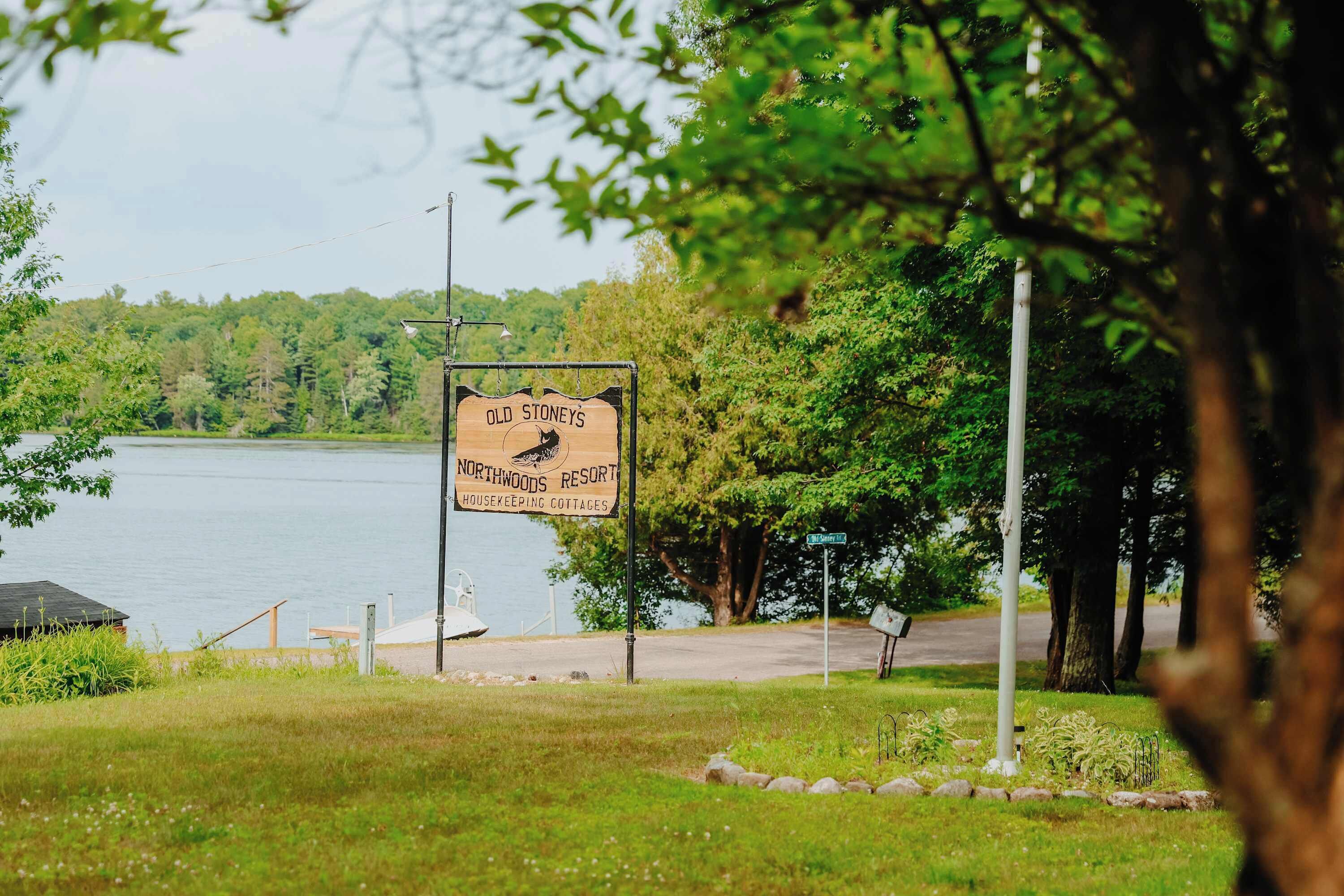 A sign for Old Stoney's Northwoods Resort Housekeeping Cottages with a view of a lake and trees.