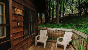 A wooden deck with two Adirondack chairs, a wooden sign with the word "Bass," and a wooden fence surrounding a lush green garden. - Old Stoney's Bass (Woodruff)