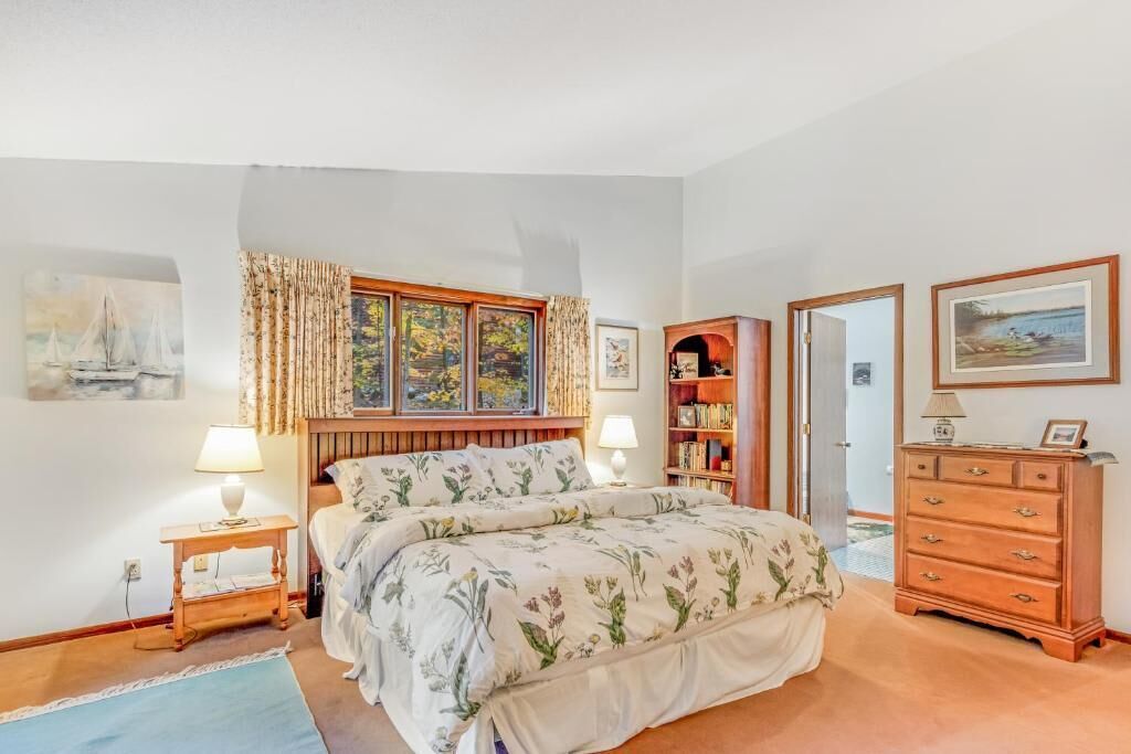 A bedroom with a bed, two bedside tables, a nightstand, a dresser, a bookshelf, and a window with curtains.