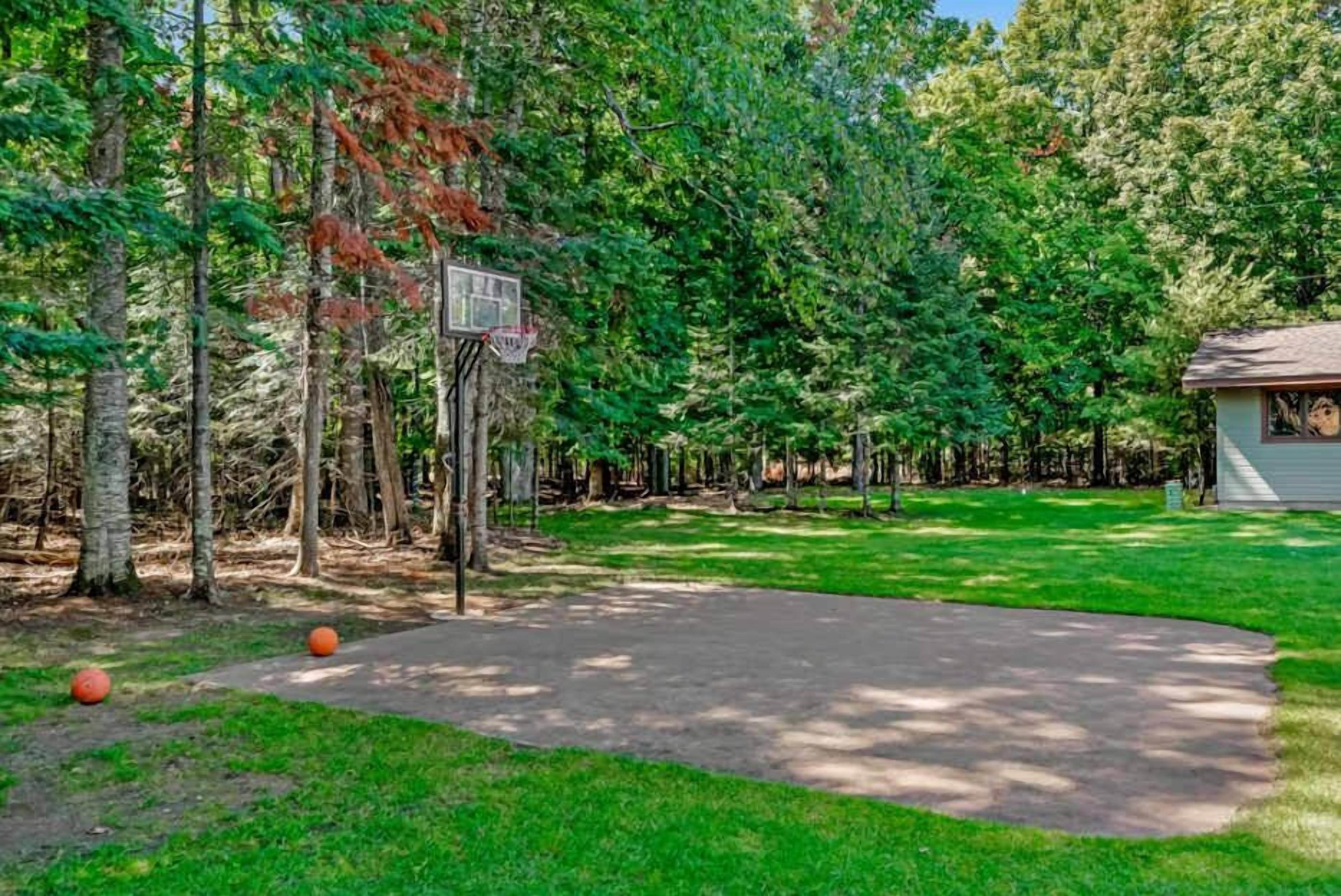 A basketball court surrounded by trees, with a small building in the background.