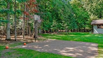 A basketball court surrounded by trees, with a small building in the background.
