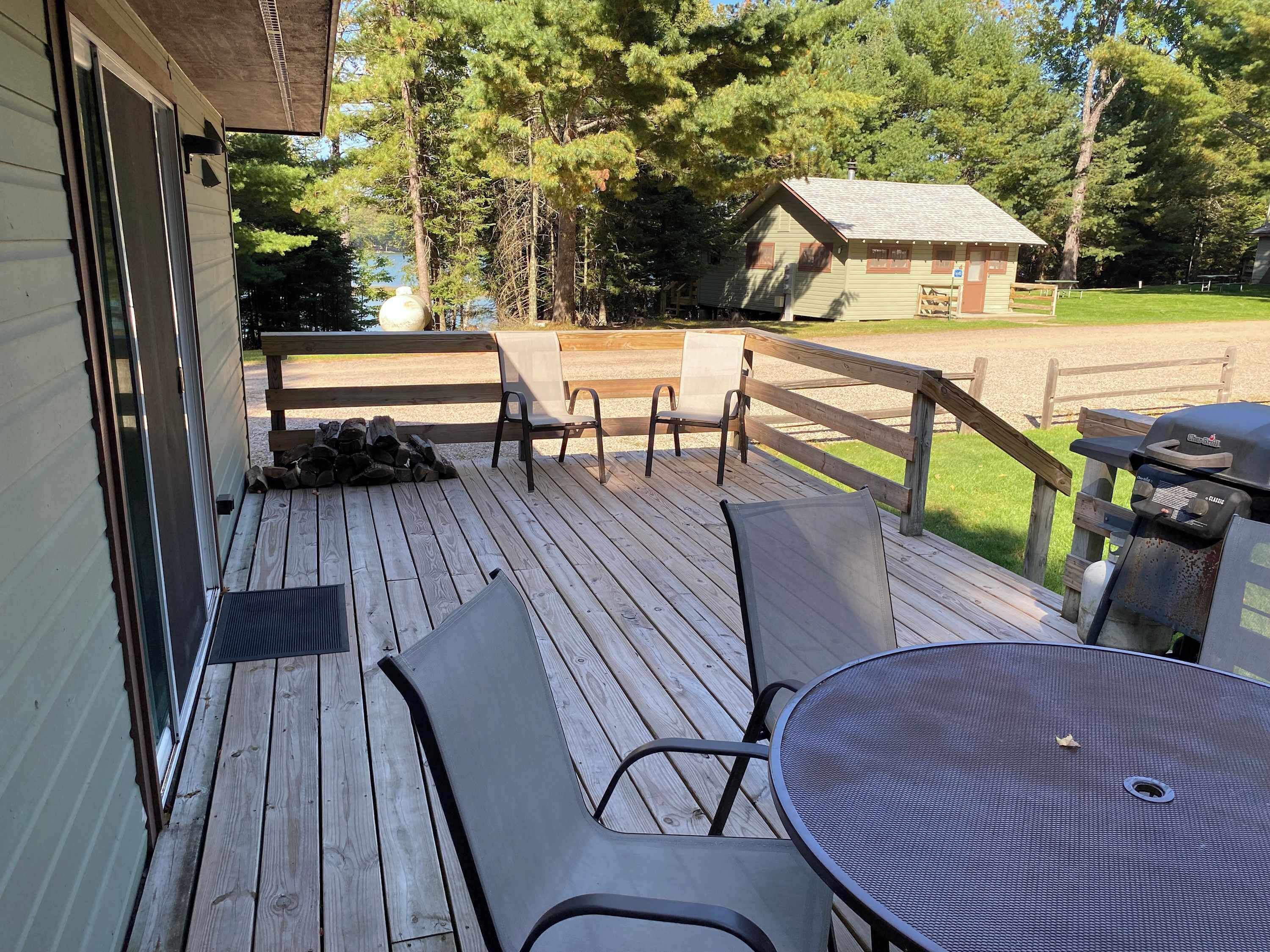 Une terrasse en bois avec une table et des chaises, un barbecue et un petit bâtiment en arrière-plan.