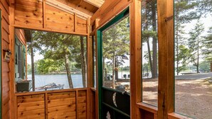 A cabin with a large window overlooking a lake, wooden walls, and a door with a metal gate. - Bouchard Shores Resort - Your Private Northwoods Getaway (Minocqua)