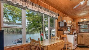 A cabin with a wooden interior, a dining table with chairs, a kitchen area, and large windows overlooking a lake. - Bouchard Shores Resort - Your Private Northwoods Getaway (Minocqua)