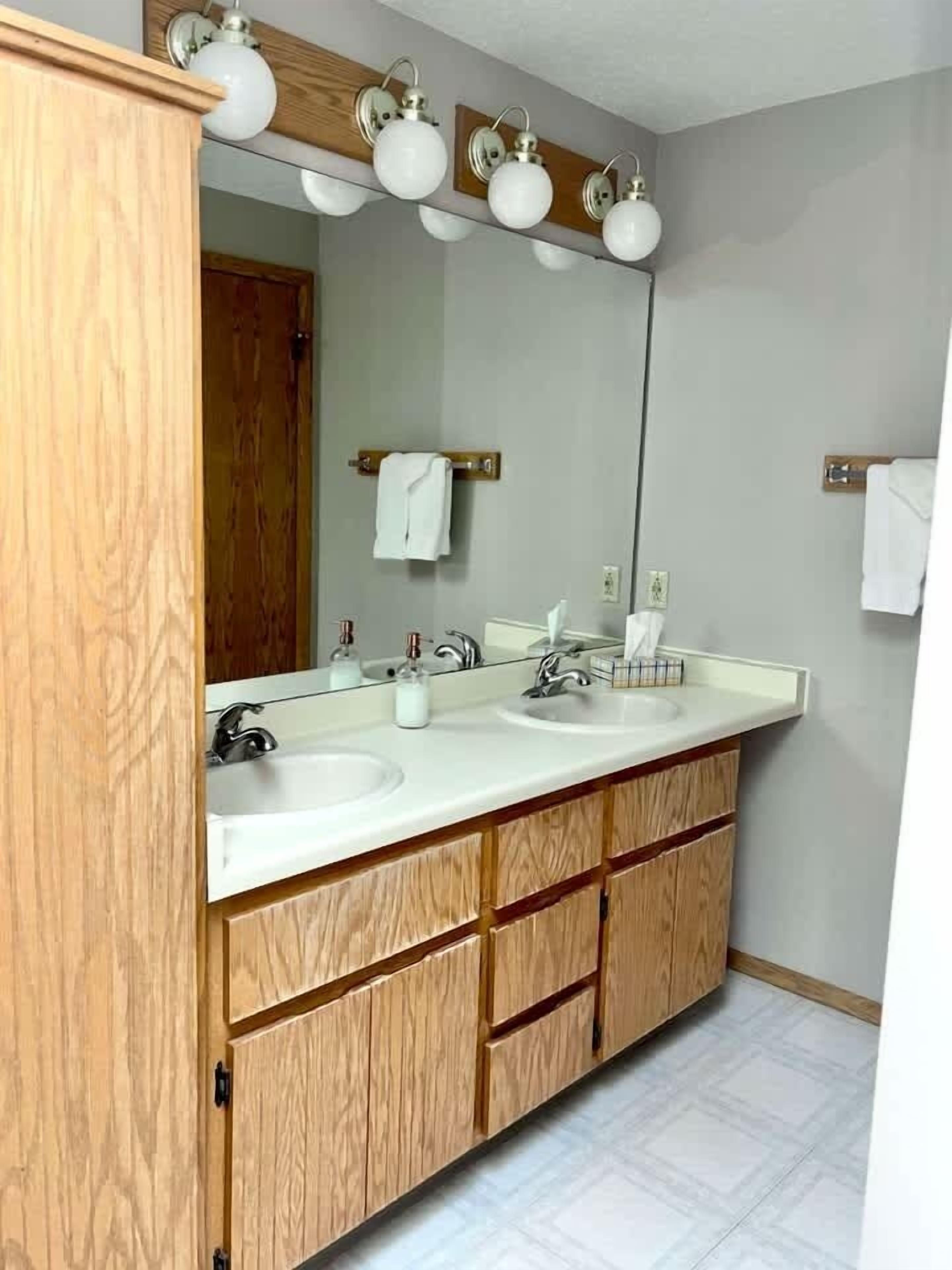 A bathroom with two sinks, wooden cabinetry, a large mirror, and a towel rack.