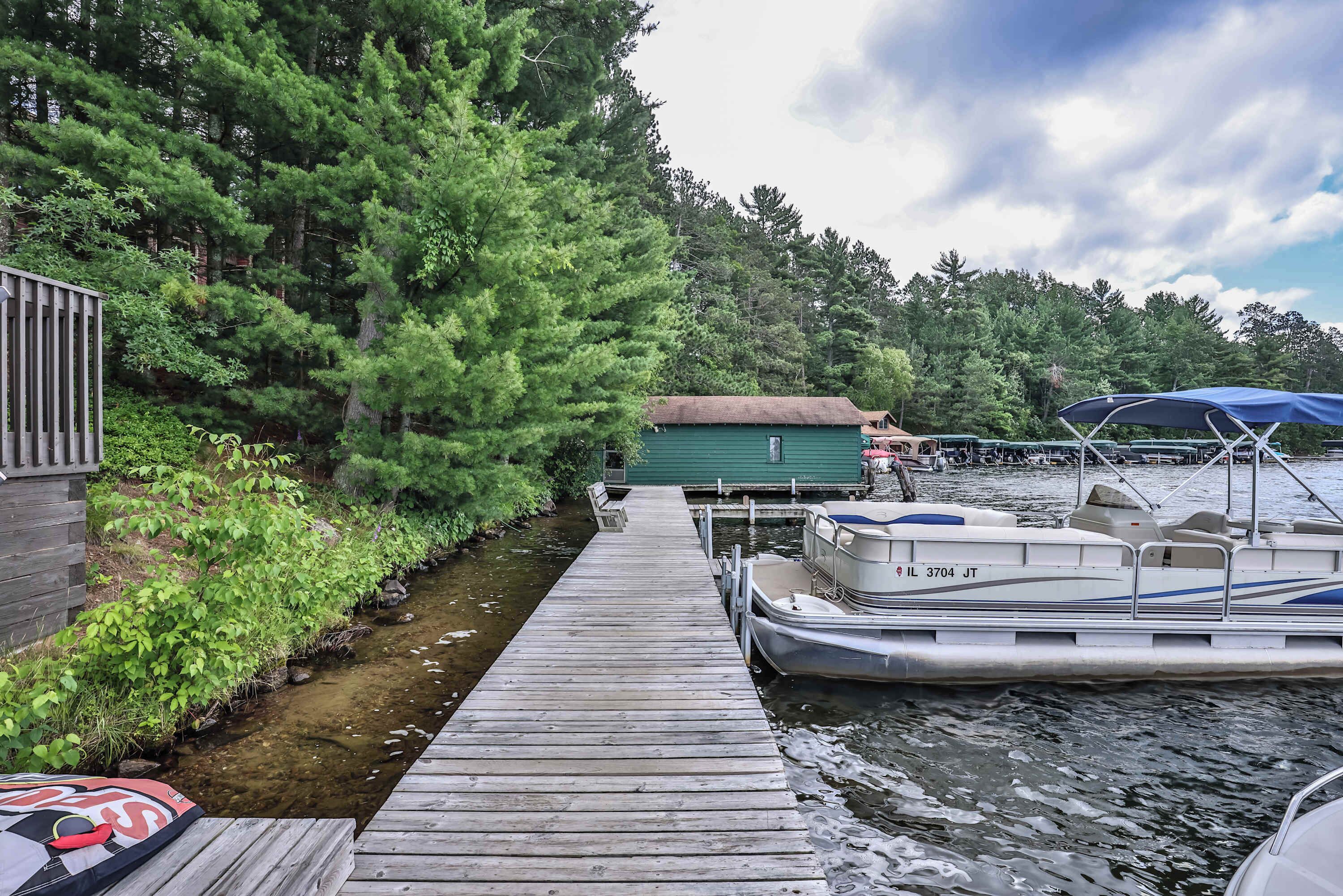 A wooden dock leading to a small house with a green roof, surrounded by dense trees.