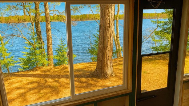 Une cabane dotée d’une grande fenêtre donnant sur un lac entouré d’arbres.