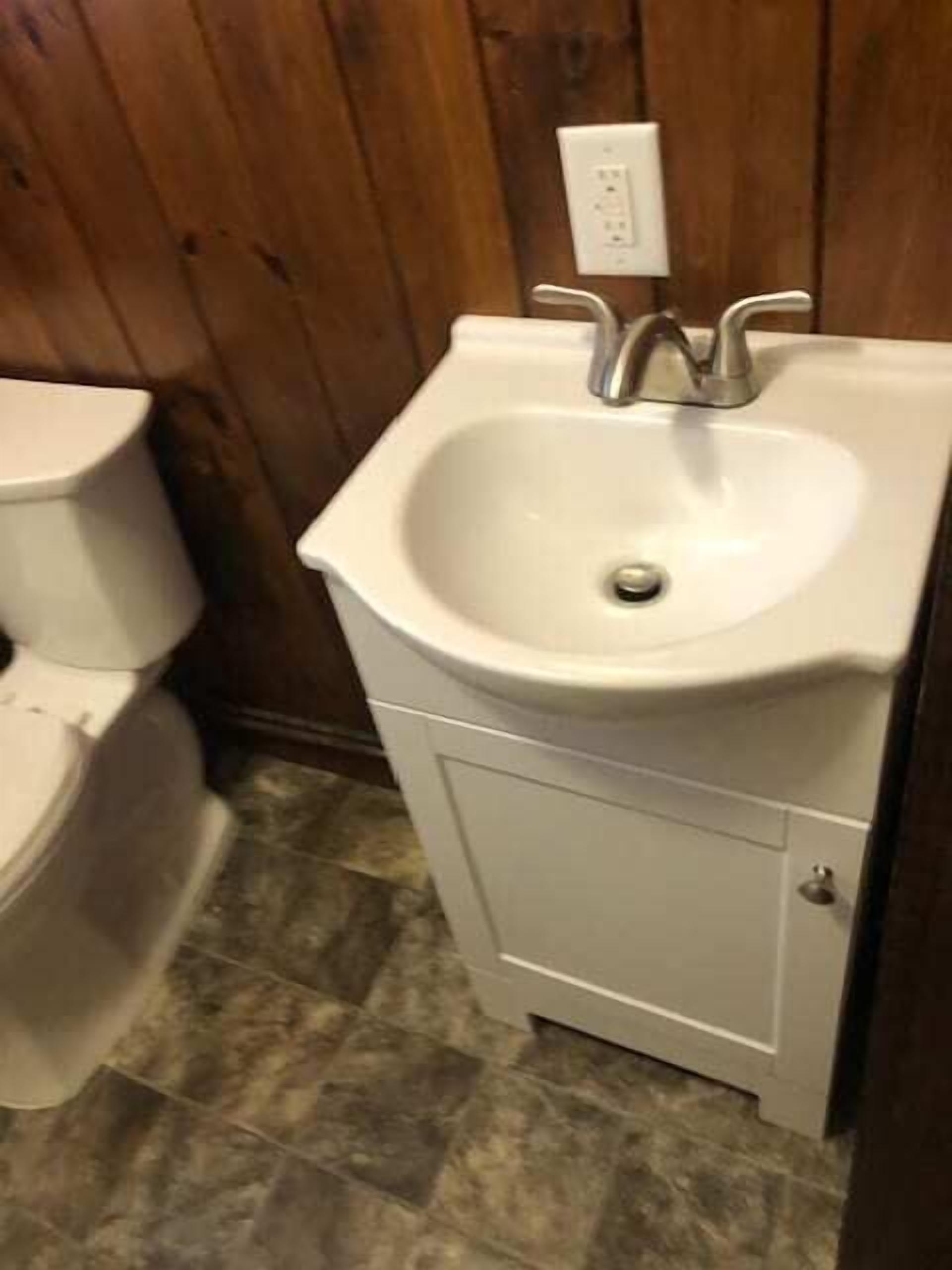 Ein Badezimmer mit einem weißen Waschbecken, einer Toilette und einer Holzwand.