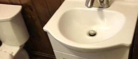 Ein Badezimmer mit einem weißen Waschbecken, einer Toilette und einer Holzwand.