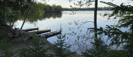 A lakeside cabin with a dock and chairs, surrounded by trees.